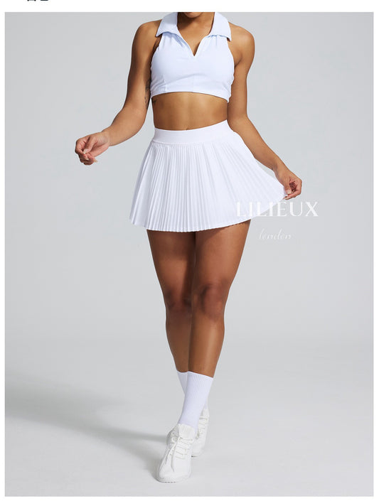 Female tennis player in a white pleated skirt and white sports bra, wearing white socks and sneakers, holding a tennis racket, showcasing a stylish and sporty look.