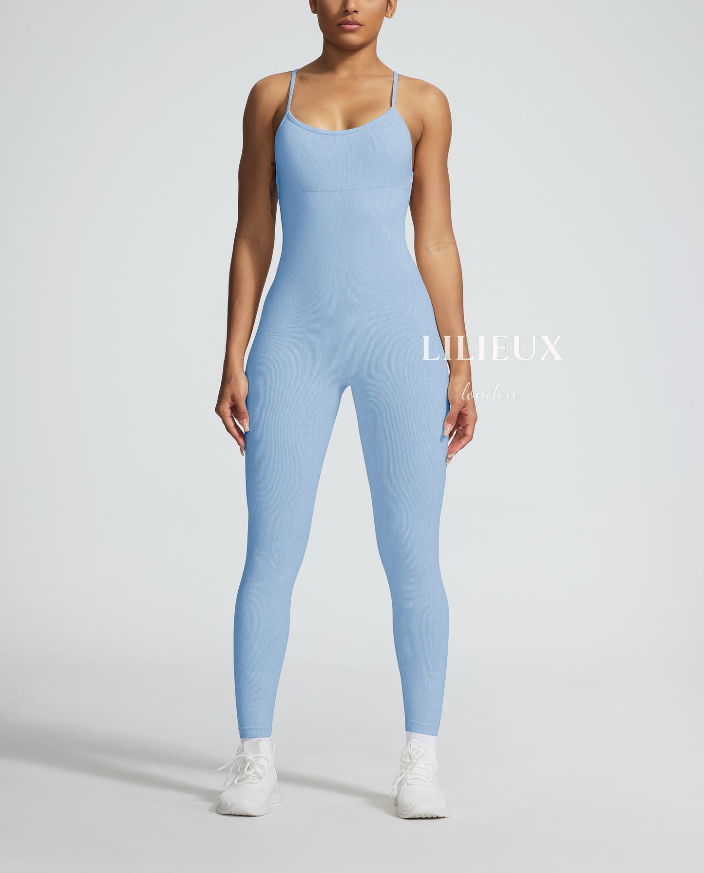 Model in a light blue graphic-patterned sports jumpsuit with thin straps, white sneakers, and socks, presenting a stylish and activewear-inspired fashion.