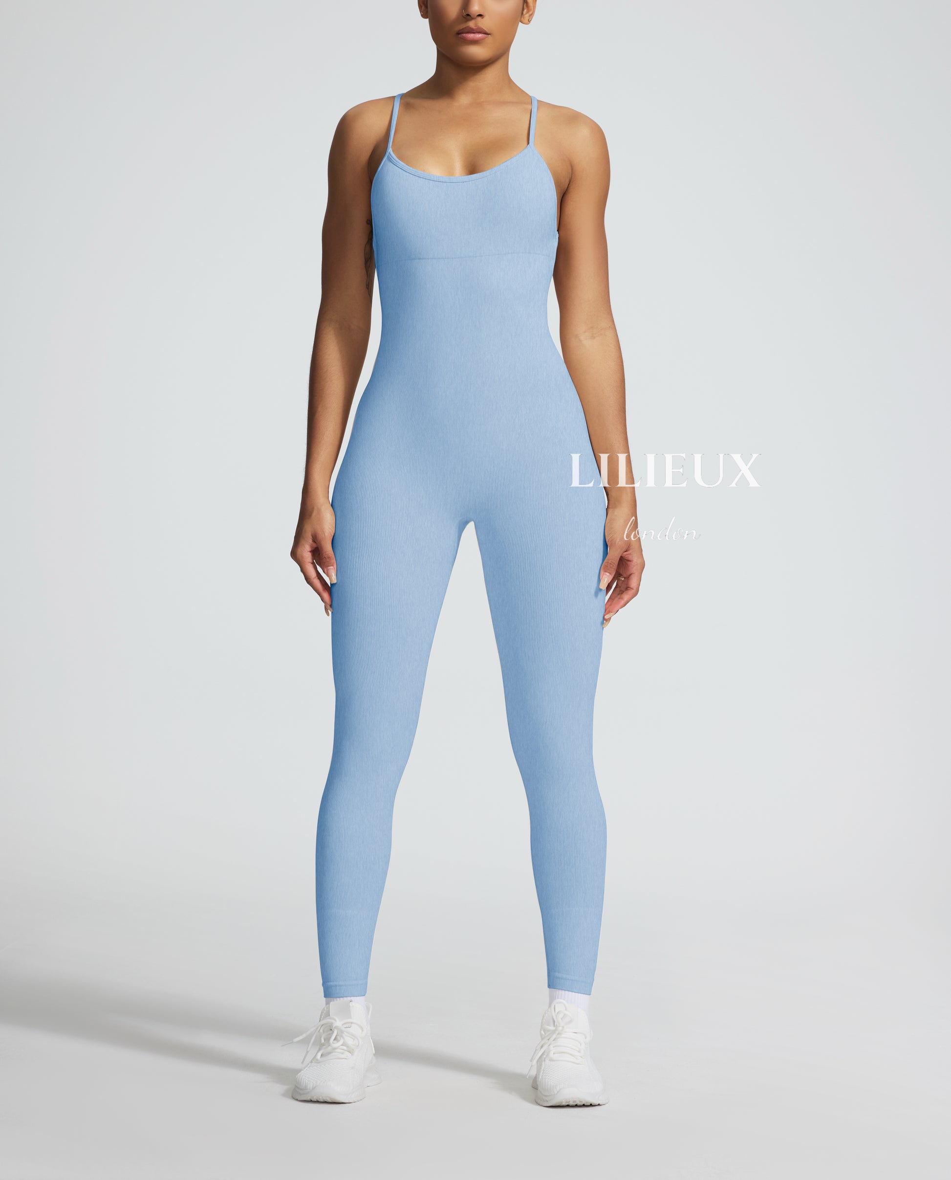 Model in a light blue graphic-patterned sports jumpsuit with thin straps, white sneakers, and socks, presenting a stylish and activewear-inspired fashion.