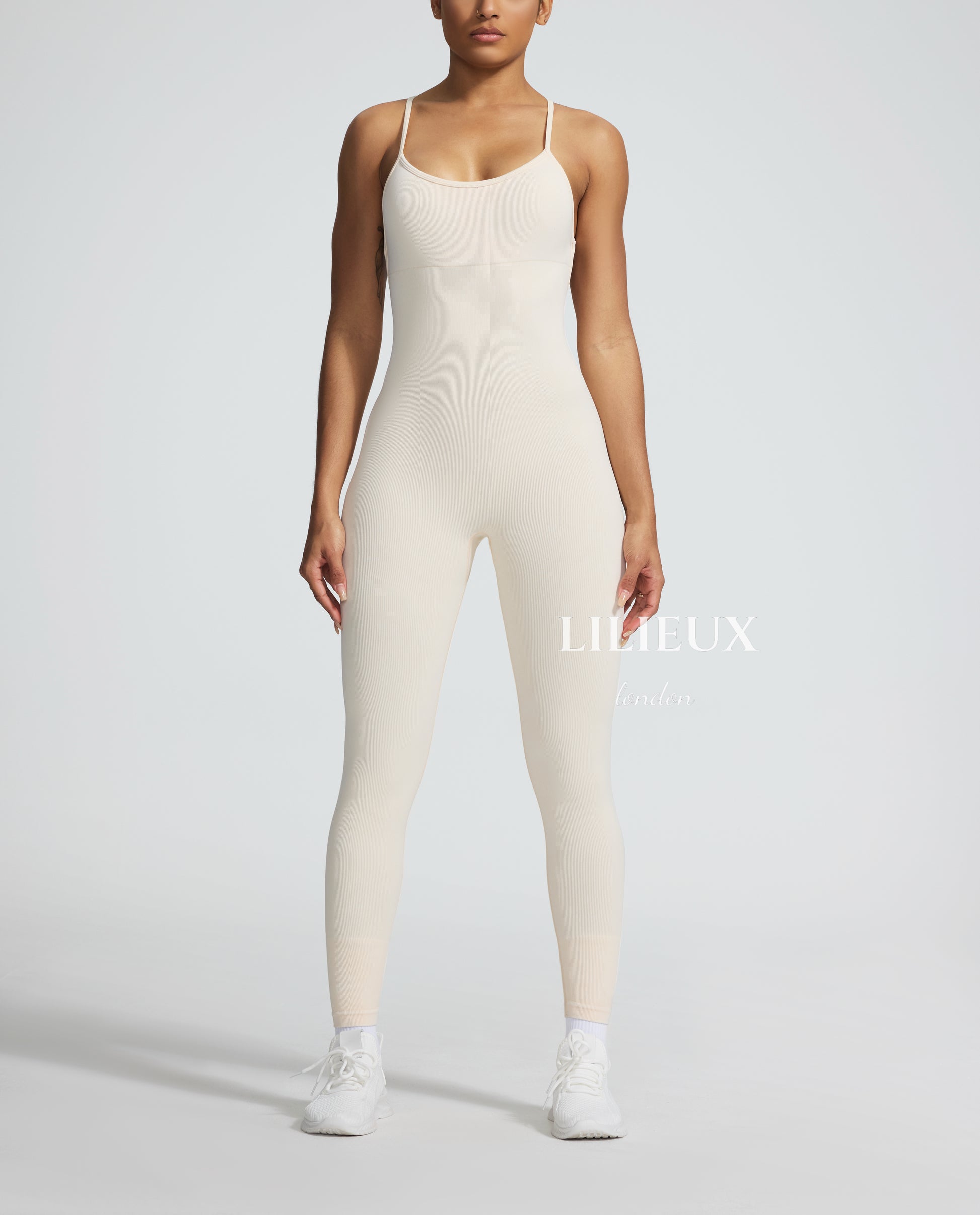 Female model wearing a cream-colored textured sports romper with thin straps, paired with white sneakers, showcasing a sleek and athletic look.