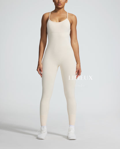 Female model wearing a cream-colored textured sports romper with thin straps, paired with white sneakers, showcasing a sleek and athletic look.