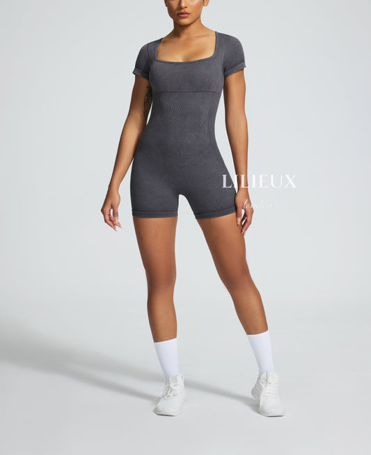 Model in a grey graphic patterned sports romper with short sleeves, white sneakers, and socks, highlighting a chic and activewear style.