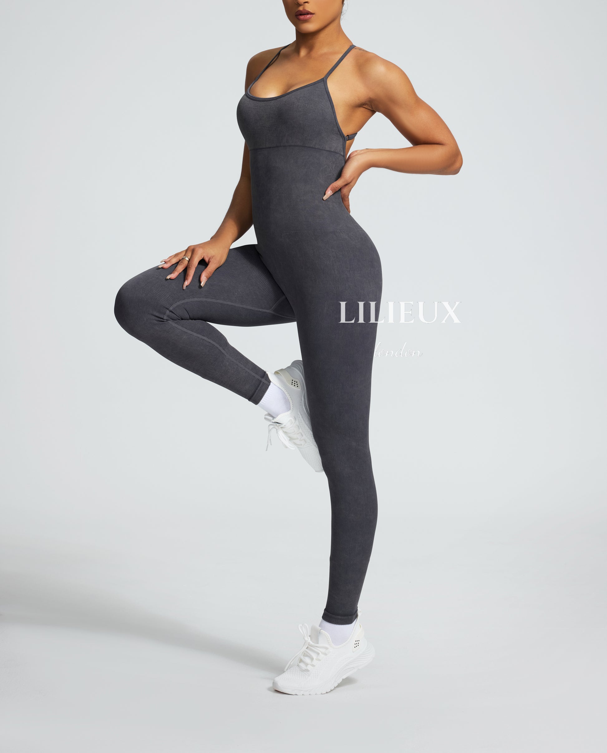 Female model wearing a grey graphic-patterned jumpsuit with spaghetti straps, paired with white sneakers and socks, showcasing a trendy and athletic style.
