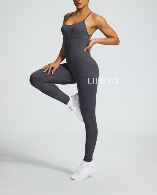 Female model wearing a grey graphic-patterned jumpsuit with spaghetti straps, paired with white sneakers and socks, showcasing a trendy and athletic style.
