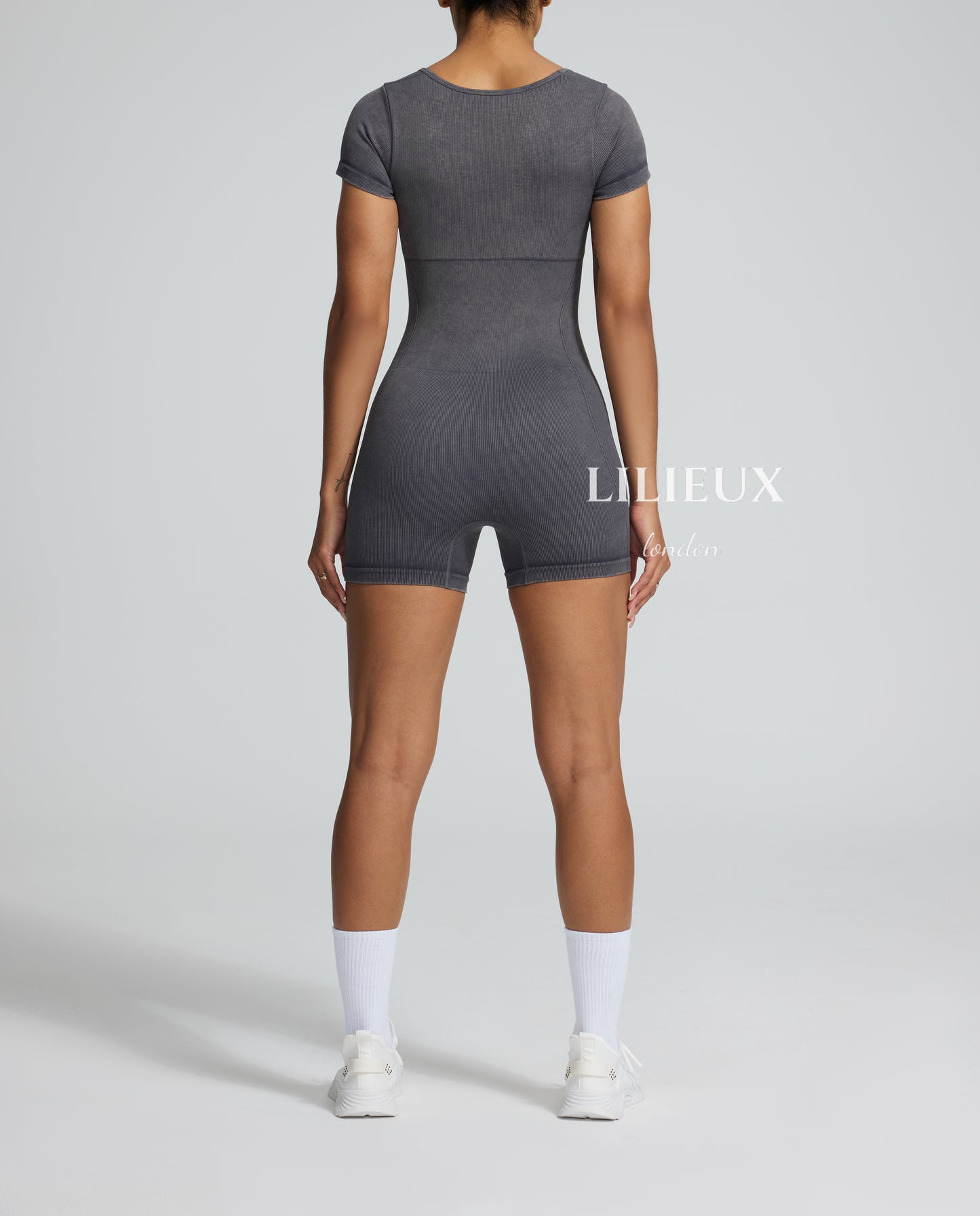 Model from the back in a grey graphic patterned sports romper, complete with white sneakers and socks, showcasing a trendy and activewear-inspired style.
