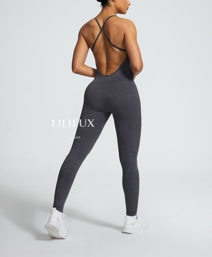 Model from the back in a grey graphic sports jumpsuit with crisscross straps and a textured design, paired with white sneakers, presenting a stylish and activewear-inspired look.