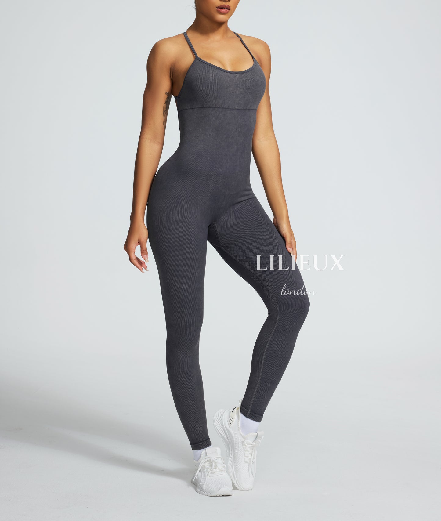 Model in a grey graphic-patterned sports jumpsuit with thin straps, white sneakers, and socks, presenting a trendy and activewear-inspired fashion.