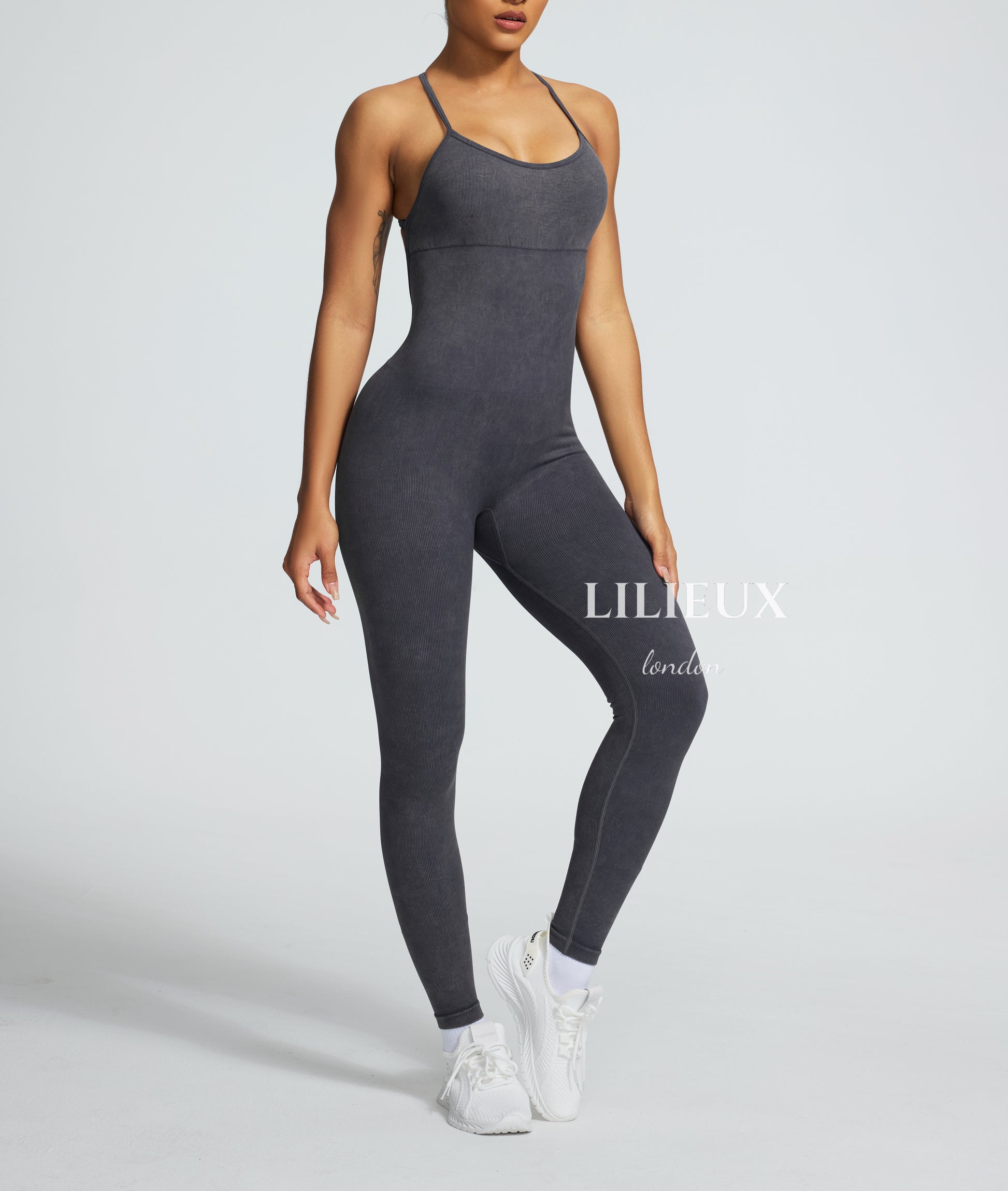 Model in a grey graphic-patterned sports jumpsuit with thin straps, white sneakers, and socks, presenting a trendy and activewear-inspired fashion.
