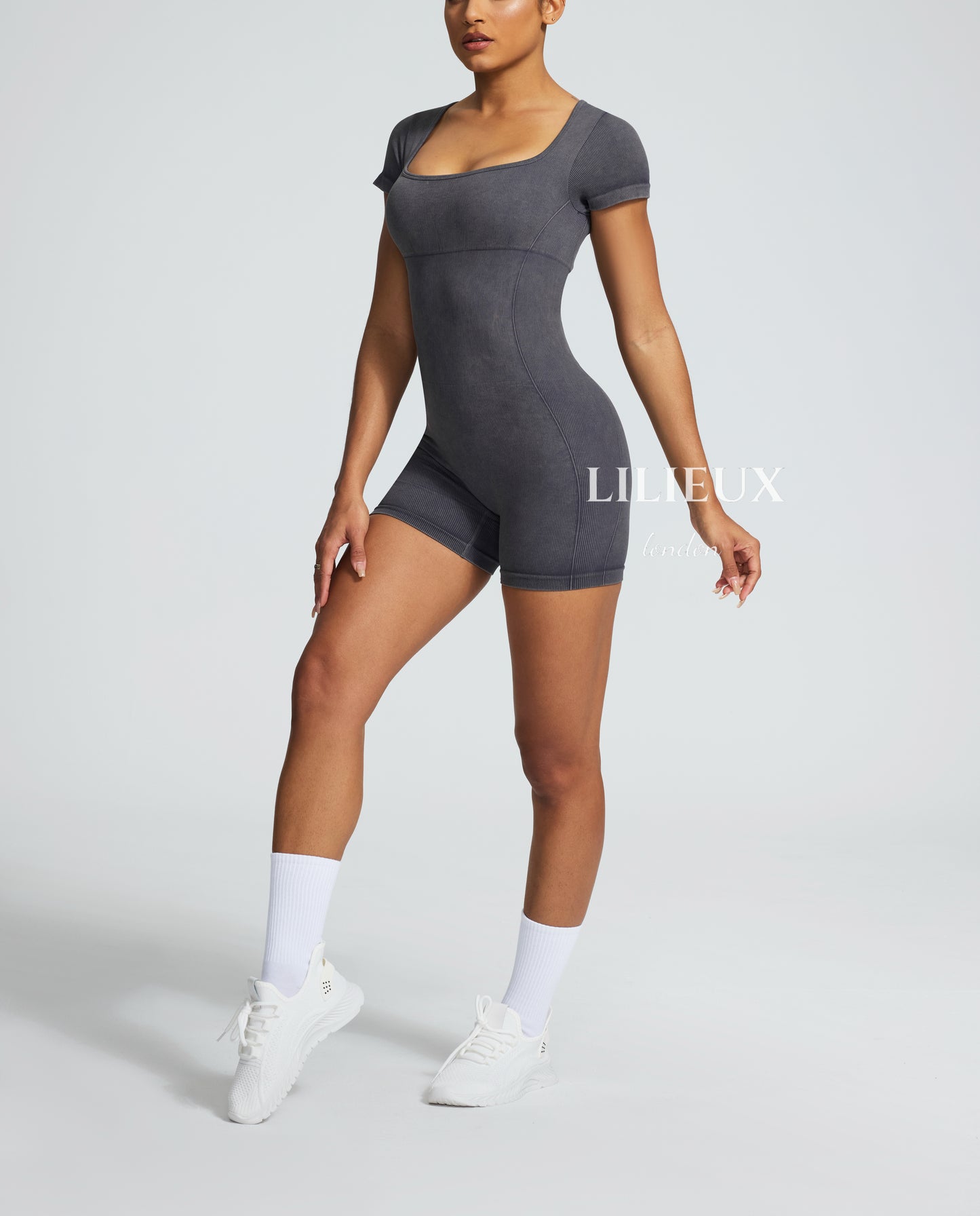 Female model in a grey printed sports romper with a graphic pattern, paired with white sneakers and socks, presenting a stylish and functional athletic look.