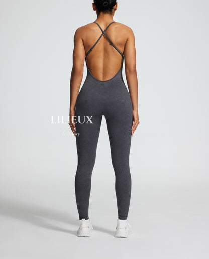 Back view of a female model wearing a grey sports romper with a crisscross back design and textured pattern, paired with white sneakers, highlighting a trendy athletic style.