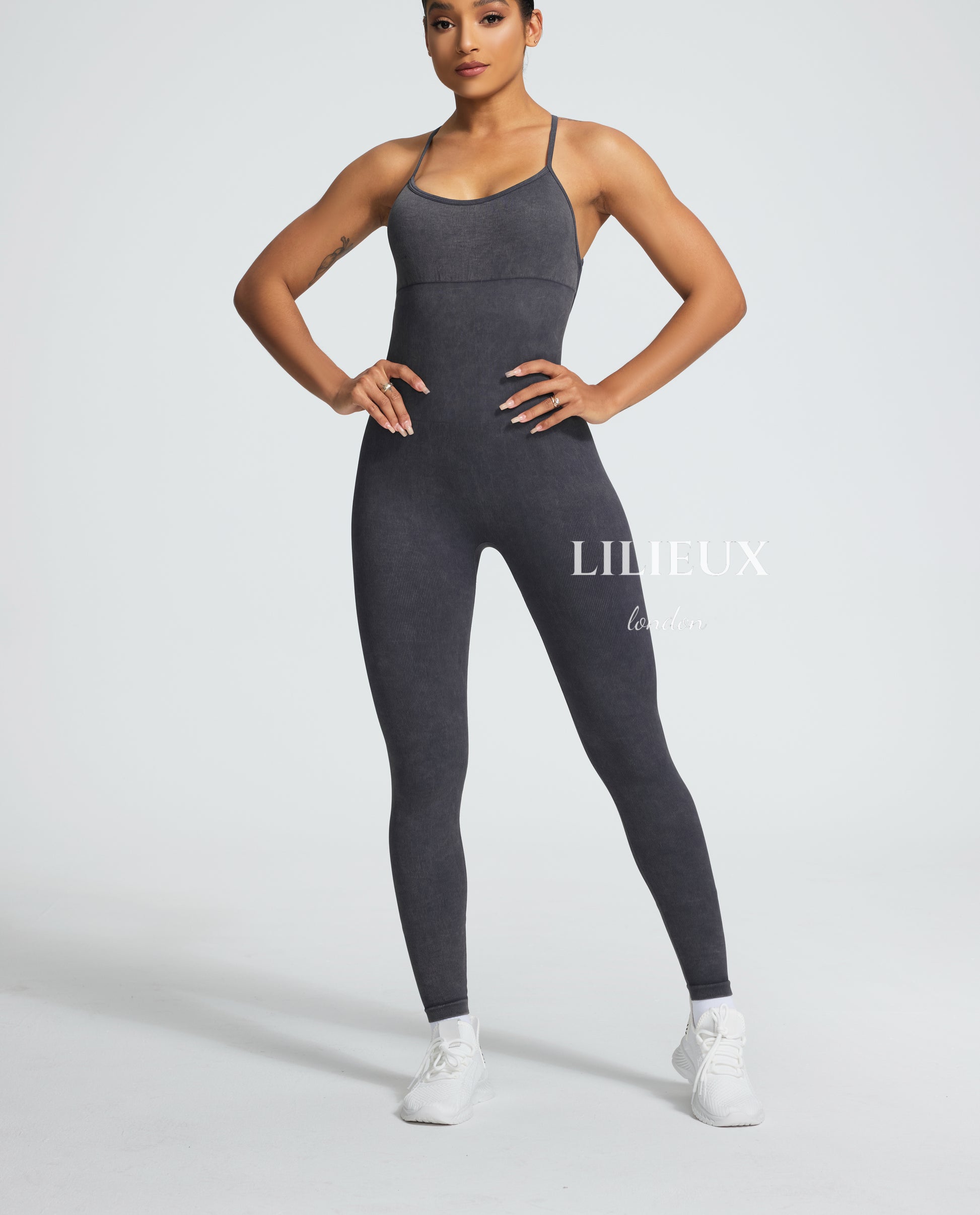 Female model wearing a grey textured sports romper with a strappy back design, paired with white sneakers, showcasing a sleek and athletic look.