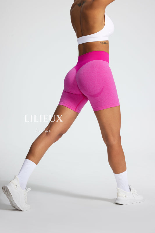 Female model wearing high-waisted pink seamless biker shorts paired with a white sports bra and white sneakers, showcasing a stylish and athletic look.