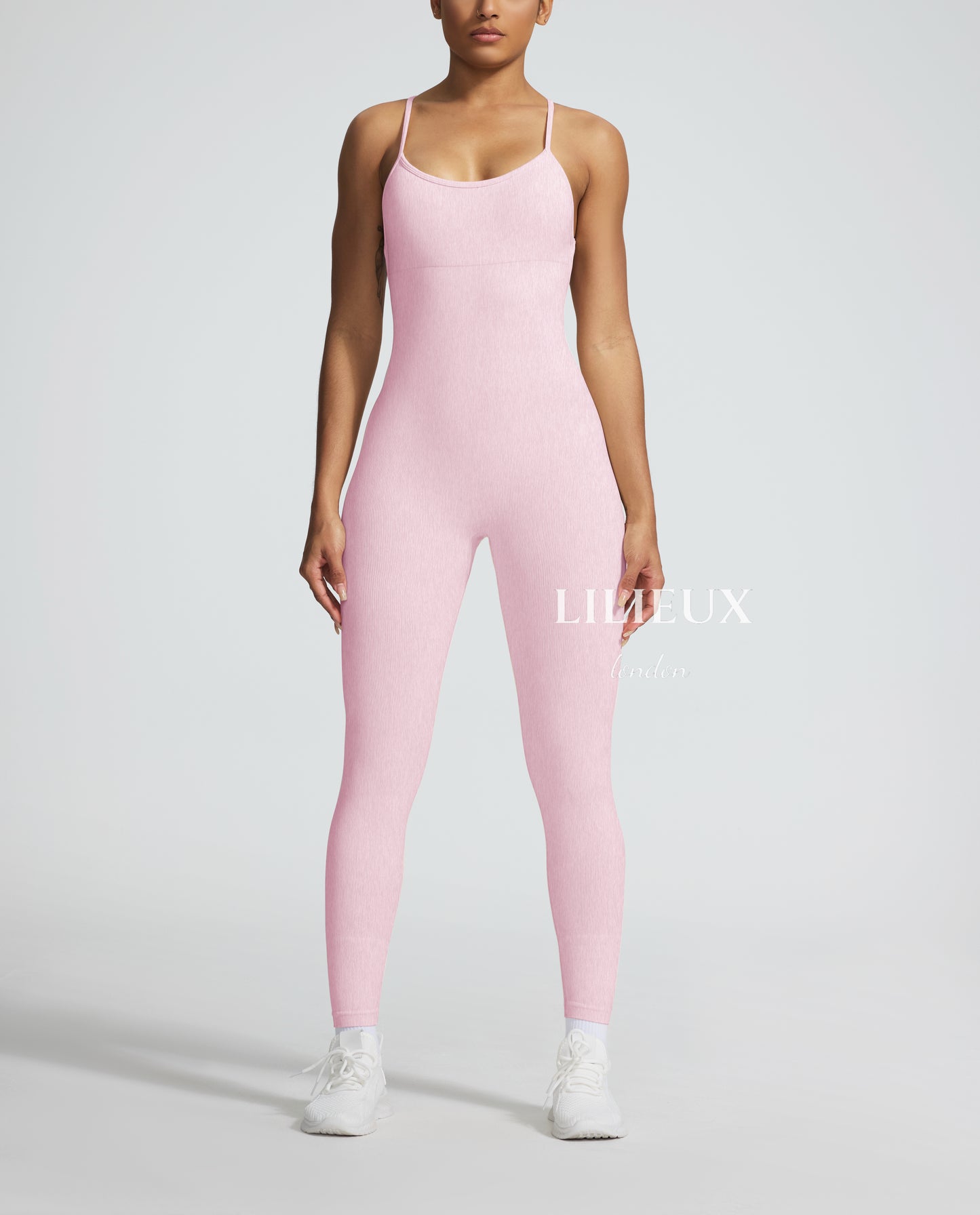 Female model wearing a pink textured sports romper with thin straps, paired with white sneakers, showcasing a sleek and athletic look.